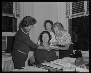 Louise Hicks in office, with three other women pinning a flower on her jacket