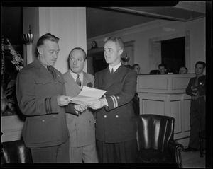 George Jessel standing between Lt. Commander Tom Collins and Lt. Joseph McDonough while they look at a document
