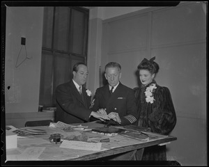 George Jessel getting fingerprinted by a uniformed officer while and his wife, Lois Andrews, looks on