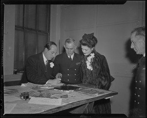 George Jessel and wife, Lois Andrews, with a uniformed officer, signing a paper
