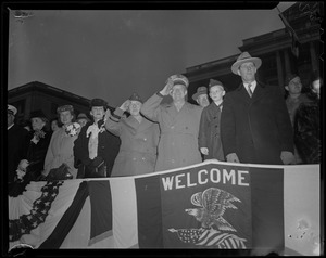 General Eisenhower salutes from a stand with welcome banner
