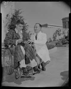 Prince Alexandre in a wheelchair, holding a box, with a doctor kneeling beside him