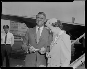Cary Grant smiling and signing an autograph for stewardess Barbara Shephard