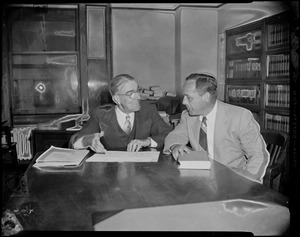 Two men sitting at a table looking at a piece of paper, most likely attorneys Baxter and St. Claire