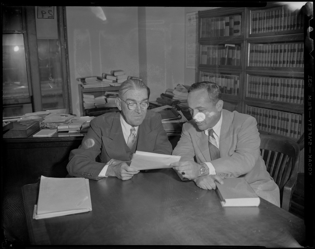 Two men sitting at a table looking at a piece of paper, most likely attorneys Baxter and St. Claire