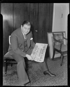 Morton Downey sitting in a chair holding a newspaper