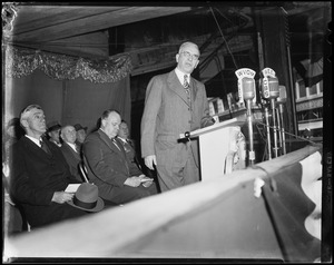 Man speaking at a podium with people sitting in the behind him