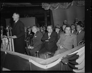 Senator Leverett Saltonstall speaking at a podium with Edward R. Mitton and Paul Dever seated at right