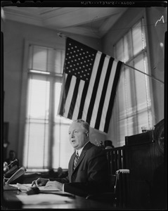 Mayor Collins at table, underneath the American flag