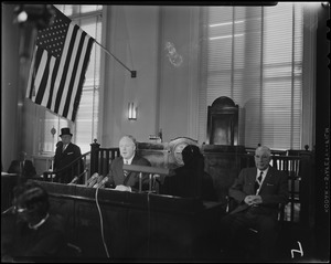 Mayor Collins at table in a courtroom with others, underneath the American flag