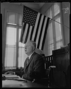 Mayor Collins at table, underneath the American flag