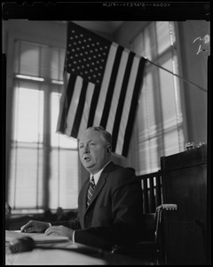 Mayor Collins at table, underneath the American flag