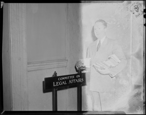 Senator John F. Collins with books in his arms and in front of the Committee on Legal Affairs sign during the State House Anti-Filthy Book Bill Hearing