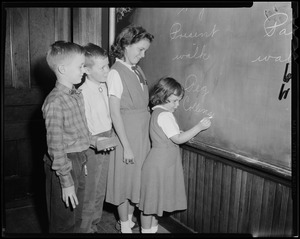 Mayor-elect John F. Collins's daughter, Peggy Collins, writing on the blackboard as siblings Thomas, Patricia, and John, Jr. look on