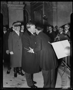 Governor James M. Curley shaking hands with another man in front of the band