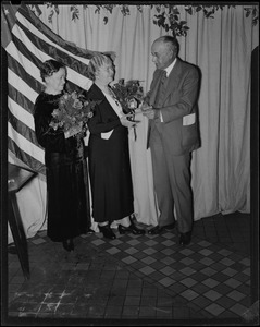 Two older woman holding flowers and receiving paperwork from an older man