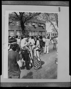 Photograph of a student seen unrolling a large American flag while striking in front of Massachusetts National Guard headquarters