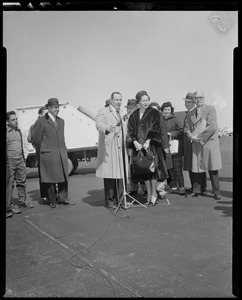 Lana Turner standing at a microphone upon arrival at Logan International Airport