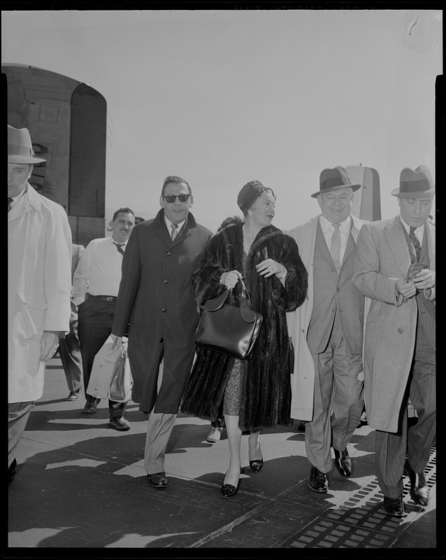 Lana Turner and a group of men walking upon arrival at Logan International Airport