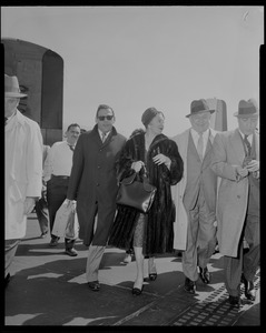 Lana Turner and a group of men walking upon arrival at Logan International Airport