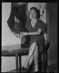 Lana Turner sitting on a table, in Boston for press interviews for newest film "Imitation of Life"