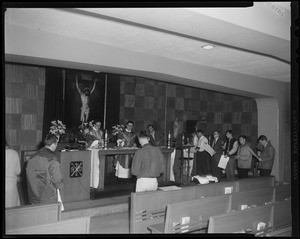 A view of people standing before an alter with two priests standing behind it