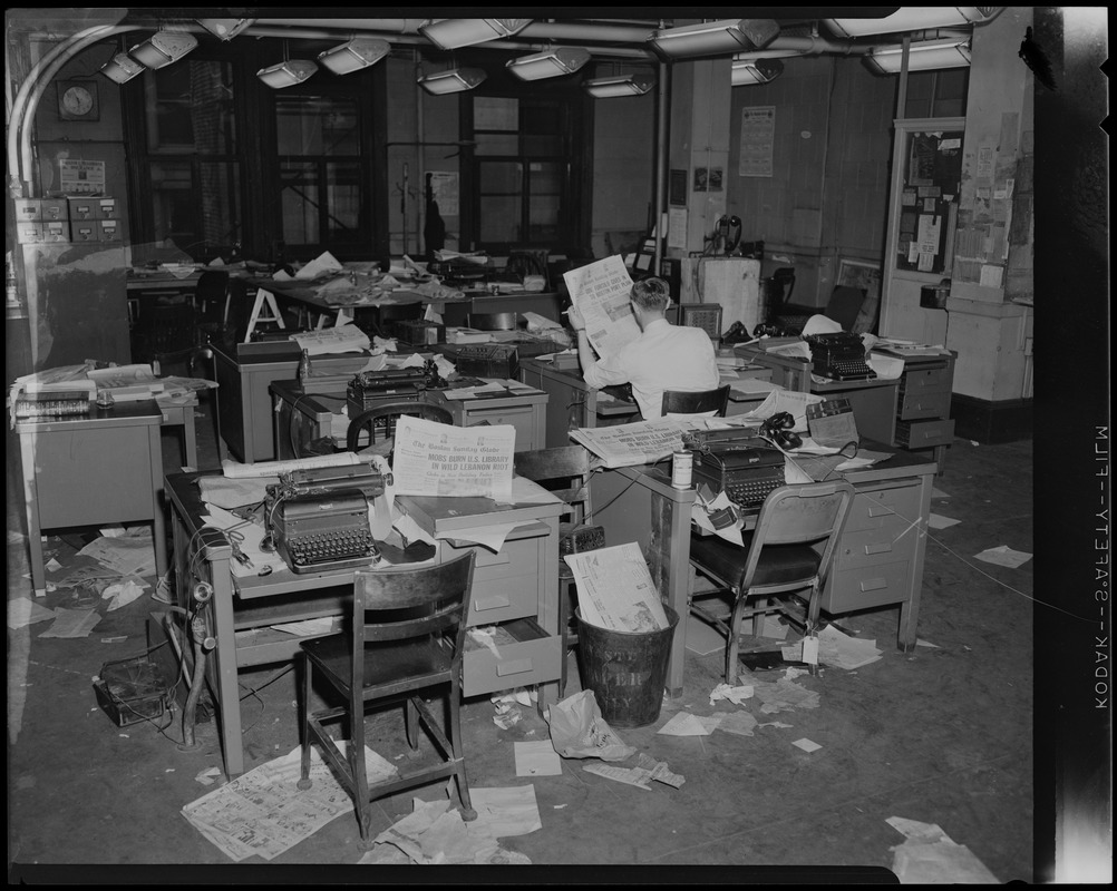 Man sitting in a disarrayed newsroom, with newspapers scattered about