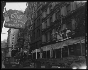 Lowering machinery out of the Globe building as two men on a truck bed await