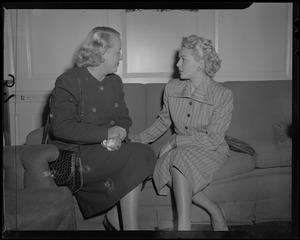 Lana Turner seated on a couch and talking with a woman