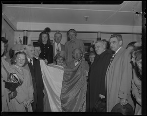 Cardinal Cushing posing with Mayor Curley, left, and a group as two people hold a flag