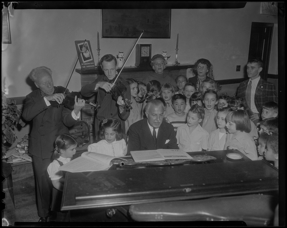 Arthur Fiedler (at piano), abetted by Inar Hanson, left, and George Zasowsky, members of Boston Symphony Orchestra, supply the musical accompaniment for these youngsters enjoying annual Christmas party at the Prendergast Preventorium, Mattapan