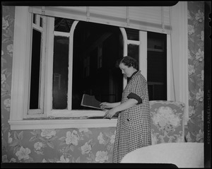 A woman holding a piece of glass beside a broken window