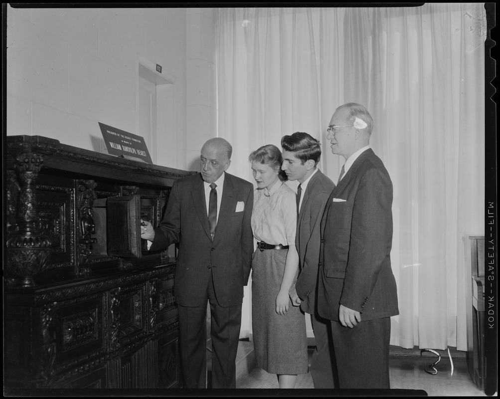 Harold G. Kern of Hearst Corp. with two young people and Rev. Dr. Harold C. Case, BU President, opening a door on a furniture piece