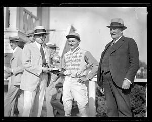 A jockey being handed a trophy by two men