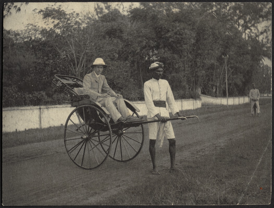 Man in pith helmet sitting in rickshaw pulled by Indian man in turban