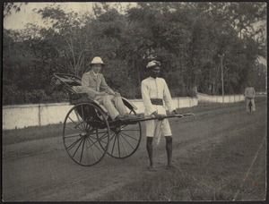 Man in pith helmet sitting in rickshaw pulled by Indian man in turban