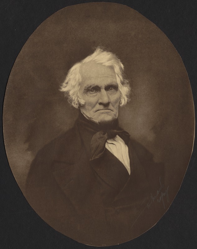 Early photo of older man in with white hair, wearing dark suit with high collar