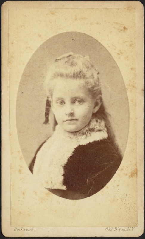 Young girl with long blond ringlets, dark frock with long white collar (head and shoulders)