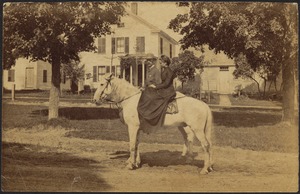 Woman and man on horseback in street in front of white house