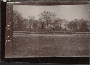 View of field with white fence, house in distance