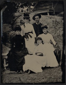4 women and 1 man sitting on rocks near cabin