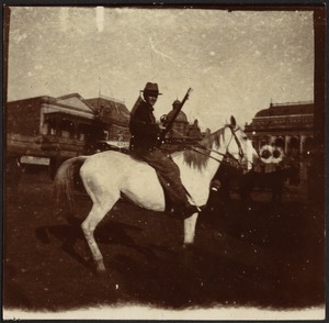 Calvary office holding rifle on horseback, riding in city street