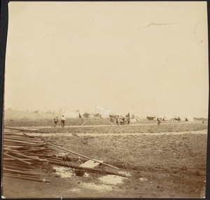 Distant view of camp, possibly a prison camp; lumber in foreground