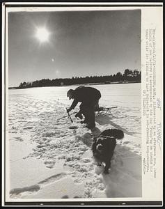 Silhouetted by an afternoon sun, James McLain of New Bedford is accompanied by his dog "Pudgy" as he checks his traps while ice fishing on Lake Snipatuit in sub-freezing temperatures.
