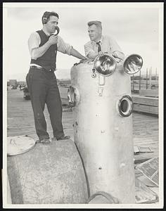 New Type Diving Bell to be Used in Search for Hidden Riches Below Sea's Surface. Los Angeles, Calif. -- Far beneath the surface of the sea, in the dark caves and submarine gardens, where men diving suits have not been able to venture, a Los Angeles inventor and deep-sea diver believes there lies a vast fortune in pearls and oyster shell. If 29-year-old William Lindley completes present plans, operation of a new type submarine diving bell in the deep pearl beds off the coast of Panama, expected to start within the next thirty days, may bring to light millions of dollars worth of heretofore unavailable pearls and shell. Lindley designed all the equipment and had charge of the diving and other operations in the raising in 1933 and 1934 of the steamship Islander, sunk in 365 feet of water in 1901 near Juneau, Alaska, with a huge cargo of gold. The new diving bell, weighing almost a ton, is cylindrical in shape, with dished ends. It is six feet four inches in height and has an inside diameter of 32-inches. There are two portholes of nine-inch diameter covered with one and one-half-inch shatterproof and bulletproof glass. The bell, with its five-eights-inch thickness of special steel in the sidewalls and seven-eights-inch thickness at the ends, will theoretically withstand a pressure equal to that encountered at 2500 feet sea depth, giving a five-to-one safety factor at 500 feet, which Lindley expats will be the maximum depth for its use in pearl-bed work. At present, a diver descends to sea bottom (at depth of about 120-feet) wearing a rubber diving suit, and with his hands picks up the oysters and loads into a basket, which when filled is hauled to the surface. These divers do not work more than a few minutes each day for fear of death from what submarine workers call "the bends." Lindley will descend in his tubular bell, and with two powerful submarine search lights will seek out colonies of oysters on the sea bottom. Even at a depth of 500 feet where the pressure is 250 pounds to the square inch, Lindley will work in comfort inside the bell under normal atmospheric pressure. As Lindley reaches sea bottom, he will give telephone orders to his mechanic assistant, who will remain on the surface to operate winches, etc. Once a colony of oysters is sighted by Lindley from the portholes of the bell, he will maneuver a large shell scoop into position and give the order for the scoop to be hoisted to the surface with the oysters it contains. A mechanical arm, controlled from within the bell, will maneuver the oyster scoop. With the oxygen tank and air purifier in the bell, Lindley can remain under water for as long as ten hours at a time. Should he encounter an accident under water, he need only release a 500-pound ballast and the bell will rise quickly to the surface. With his new type diving bell Lindley believes he can gather in excess of six tons of oyster shells in one day. -- Photo shows -- William Lindley, (right) shown with the diving bell he will use in hunting for pearls in the Pearl Islands area located west of Panama Canal. Jack Orlandi, his assistant, is seen speaking into communication phone.