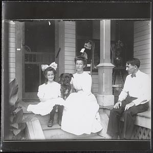 Girl, woman and man, with dog, on stoop of house