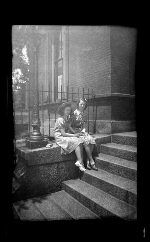 Two women, one wearing a hat, sit next to set of stairs