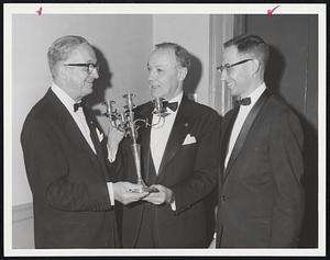 Farewell Gift of a 1788 George III silver candelabra is presented to Dr. Alfredo Trinchieri, left, who is leaving post as consul-general of Italy in Boston, by Joseph Coletti, chairman of Massachusetts Art Commission. At right is Dr. Anthony A. Abruzzese, chairman of the farewell dinner held by the Dante Alighieri Society at Harvard Club last night.