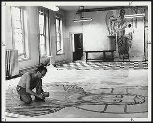 Two men painting religious figures, one on floor and one on wall