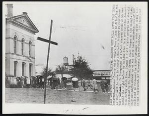 Negroes Shun Polls after Klan Demonstration--Johnson County white voters form a line in drizzling rain as they wait to vote in County Democratic Primary at courthouse here yesterday. In foreground is 15-foot charred cross which was burned the night before by Ku Klux Klan in a pre-election demonstration during which Pres. Truman’s civil rights program was sharply criticized by Dr. Samuel Green, Grand Dragon of the Georgia Klan. Only one negro showed up at the polls here yesterday, out of 240 qualified to vote--and he didn’t attempt to vote after being told he was registered.
